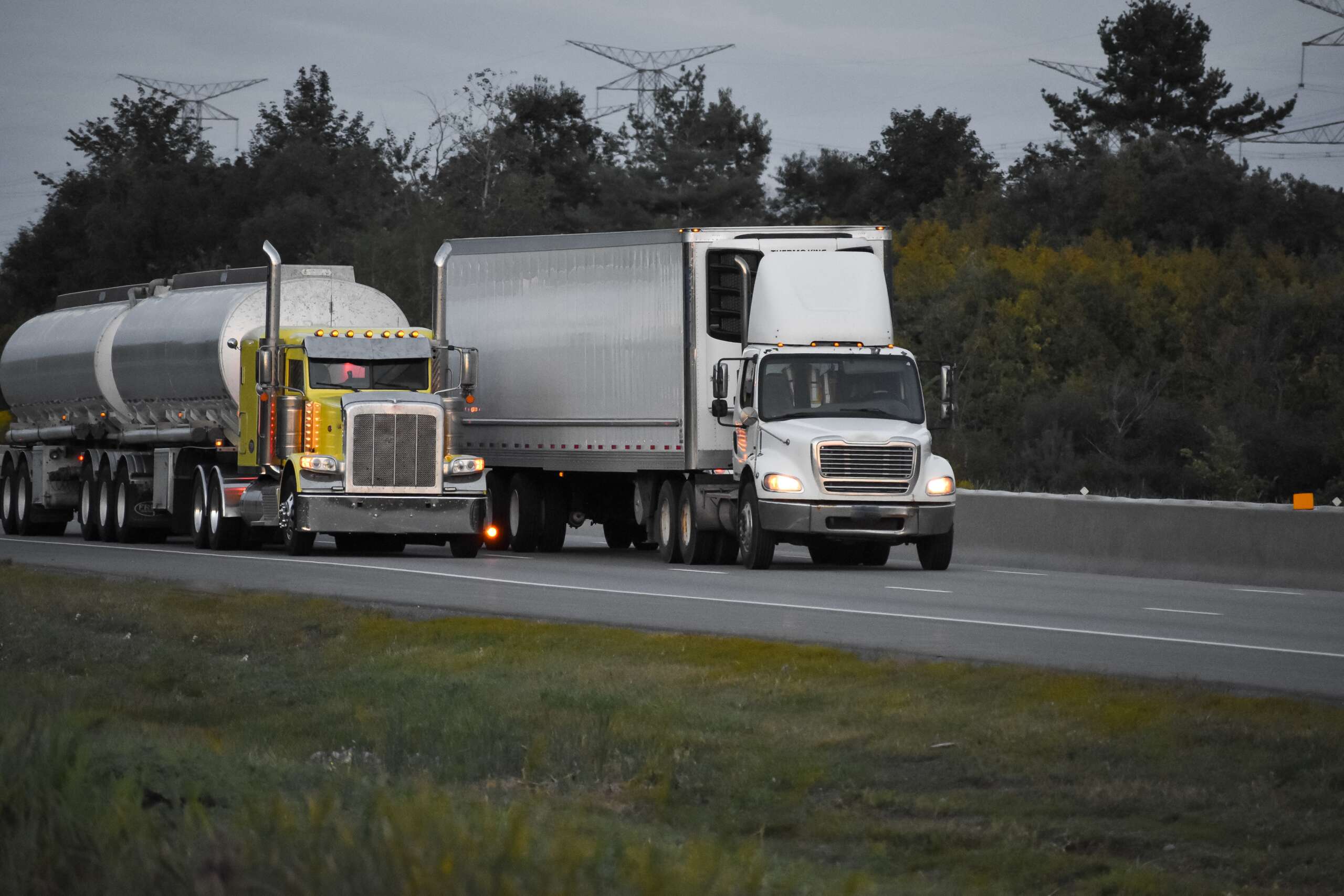 Two trailer trucks driving on the road surrounded by beautiful green trees